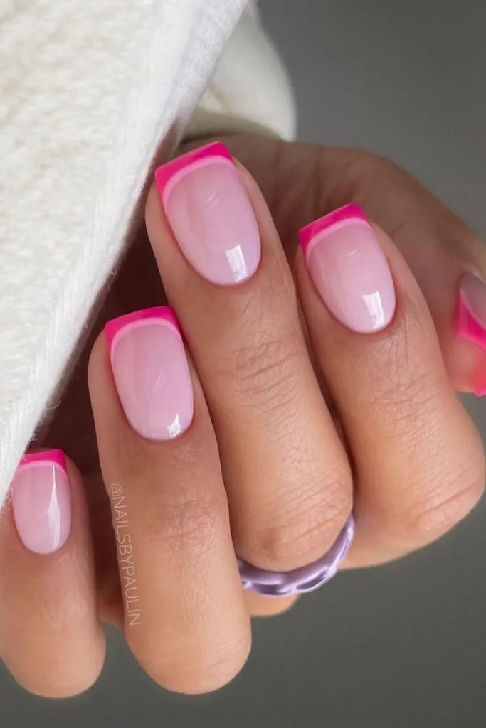 A close-up shot of a hand with manicured nails featuring a pink French tip design