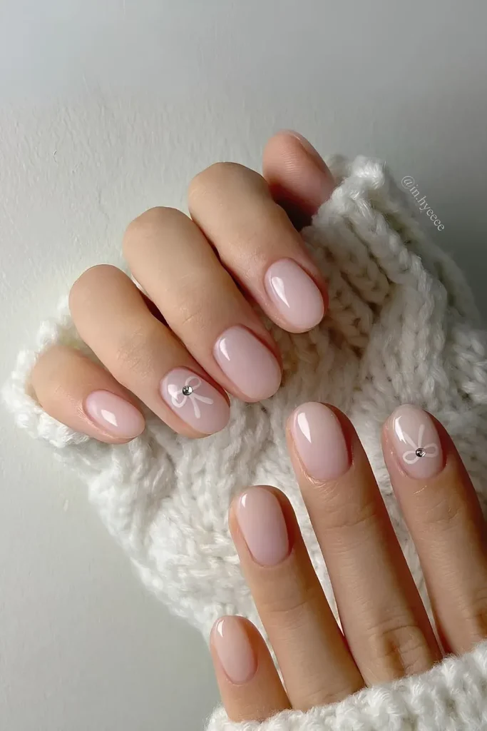 A close-up shot of a hand with pale pink manicured nails against a backdrop of a cream-colored knit sweater.