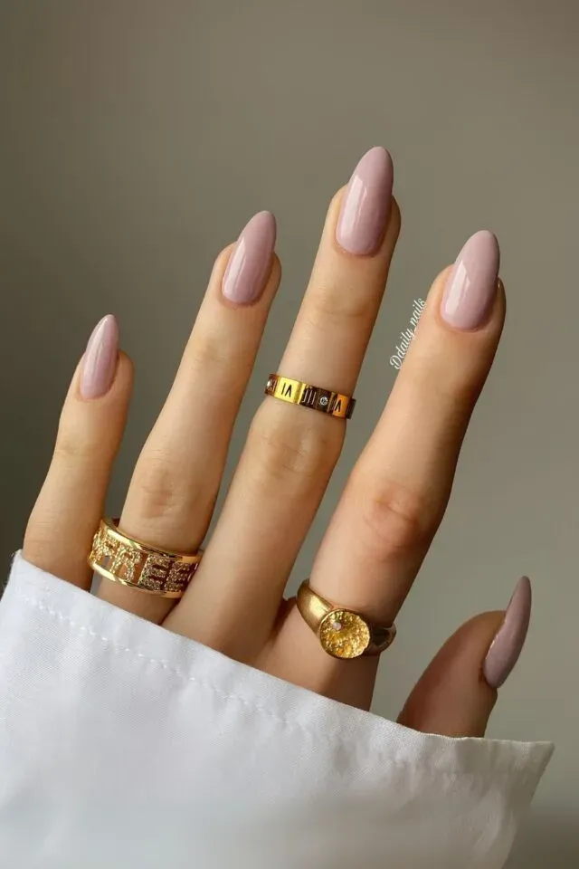 A hand with cute pink nail designs, featuring long, almond-shaped glossy pink nails paired with elegant gold rings.