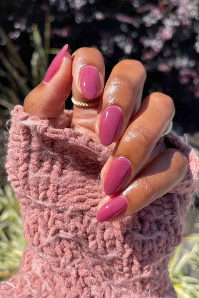 Pink jelly nails on a hand against a pink sweater.