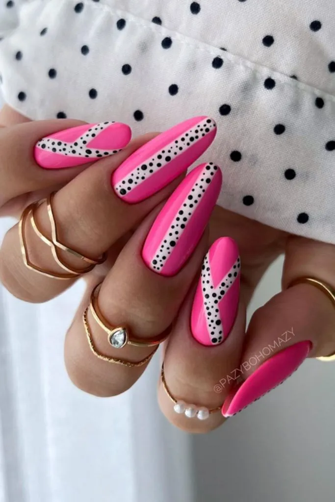 Pink nails with white stripes and black dots, gold rings on fingers.