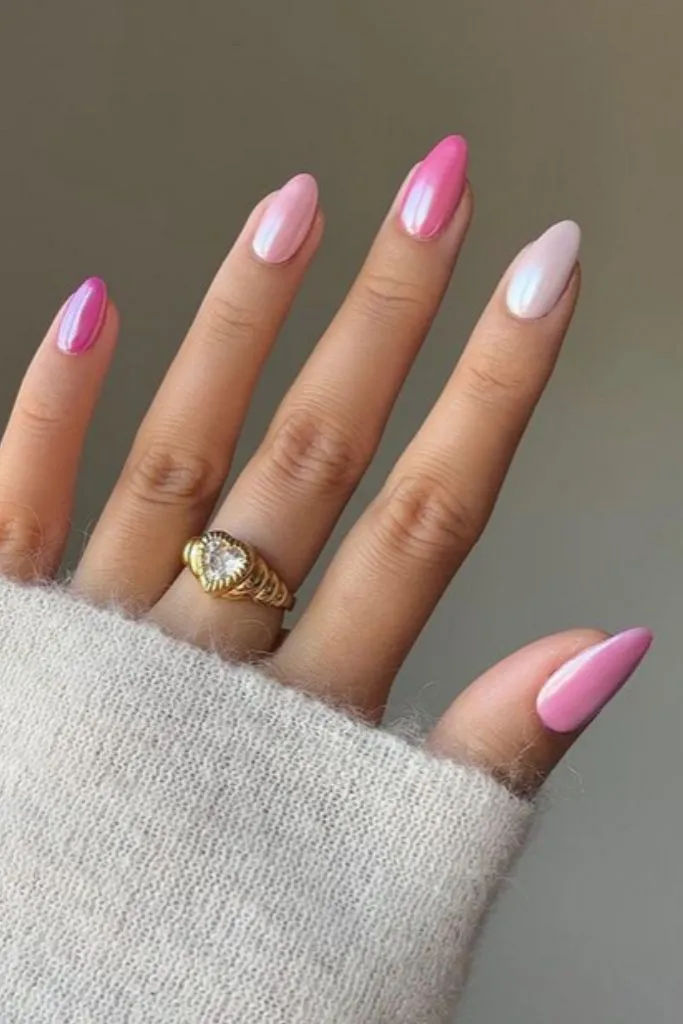 A hand with almond-shaped nails in five shades of pink chrome, creating a gradient effect.