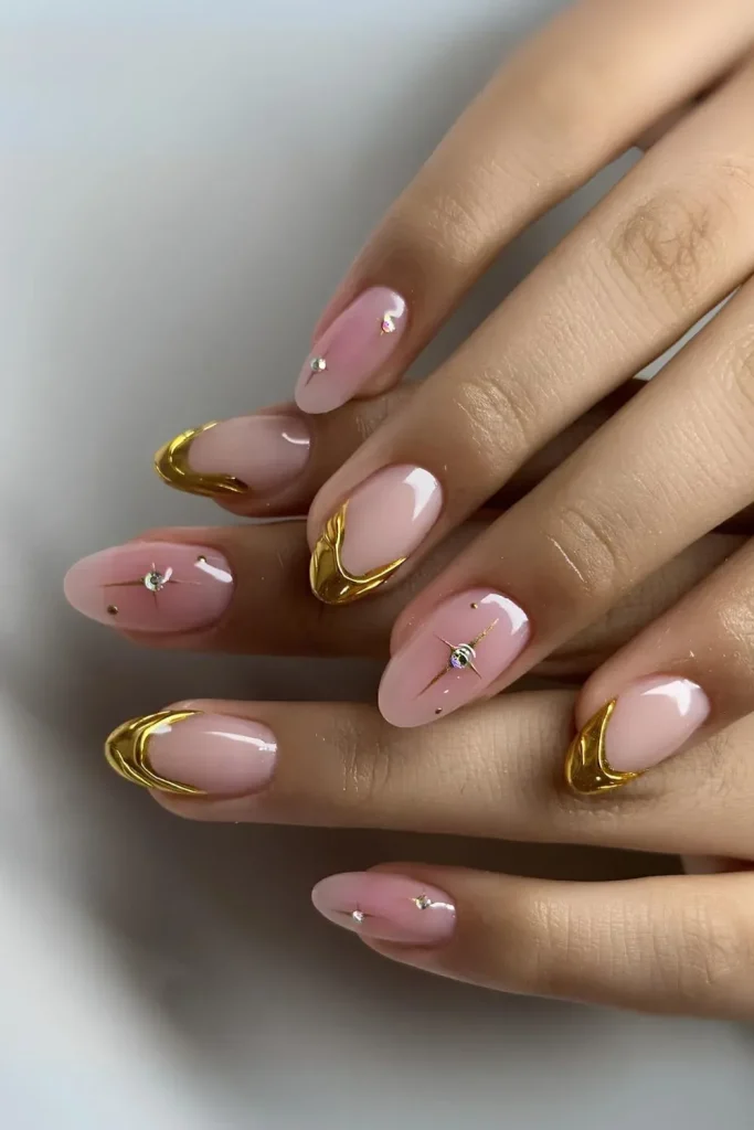 Pink nails with gold French tips and rhinestone accents.