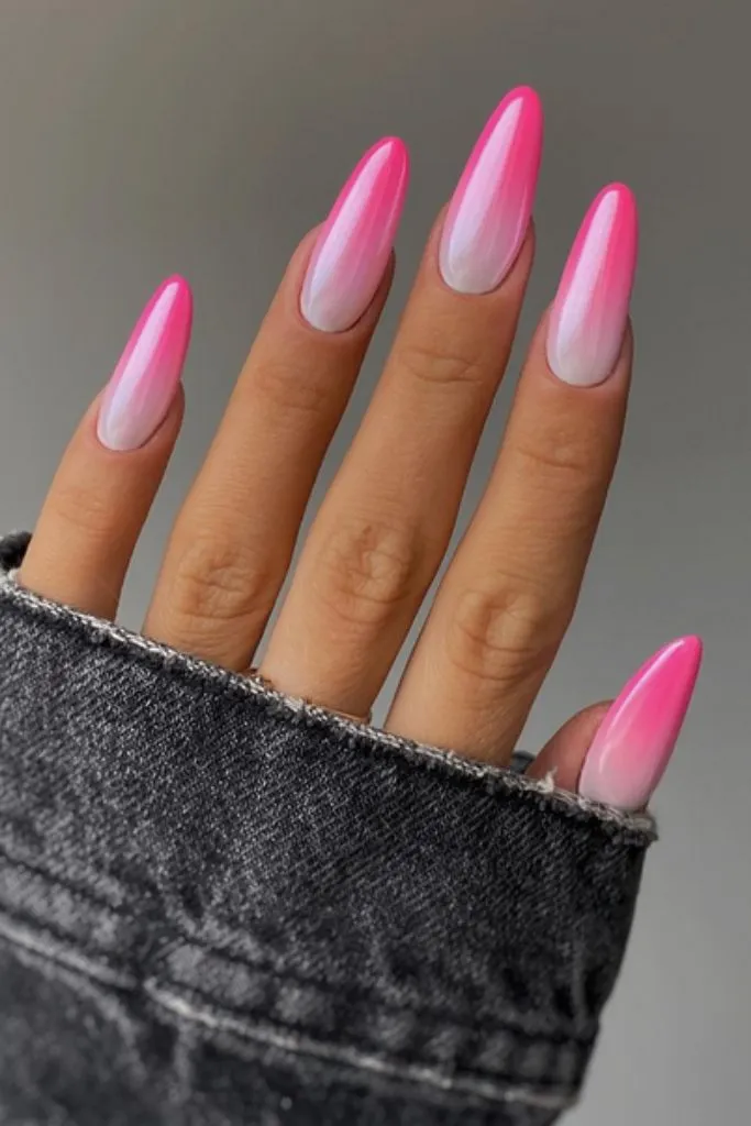 a hand with long, almond-shaped nails featuring a pink and white ombre manicure