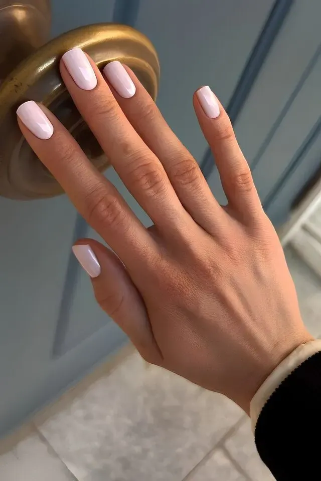 A hand with cute pink nail designs, featuring glossy, soft pink nails against a blue door handle