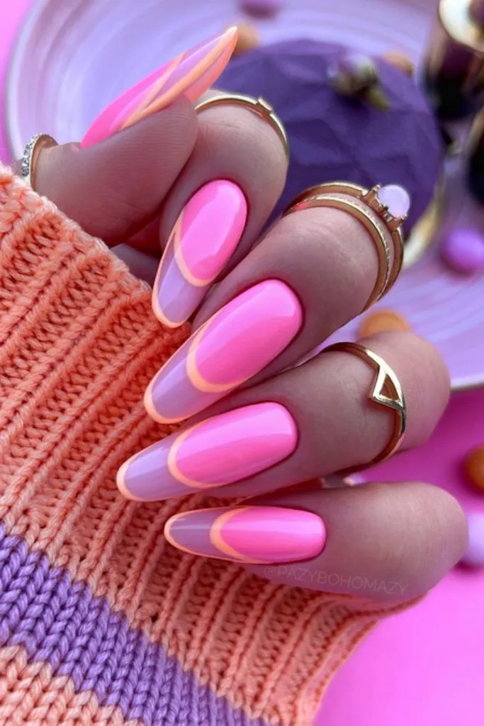 Pink French manicure with orange outline and gold rings.