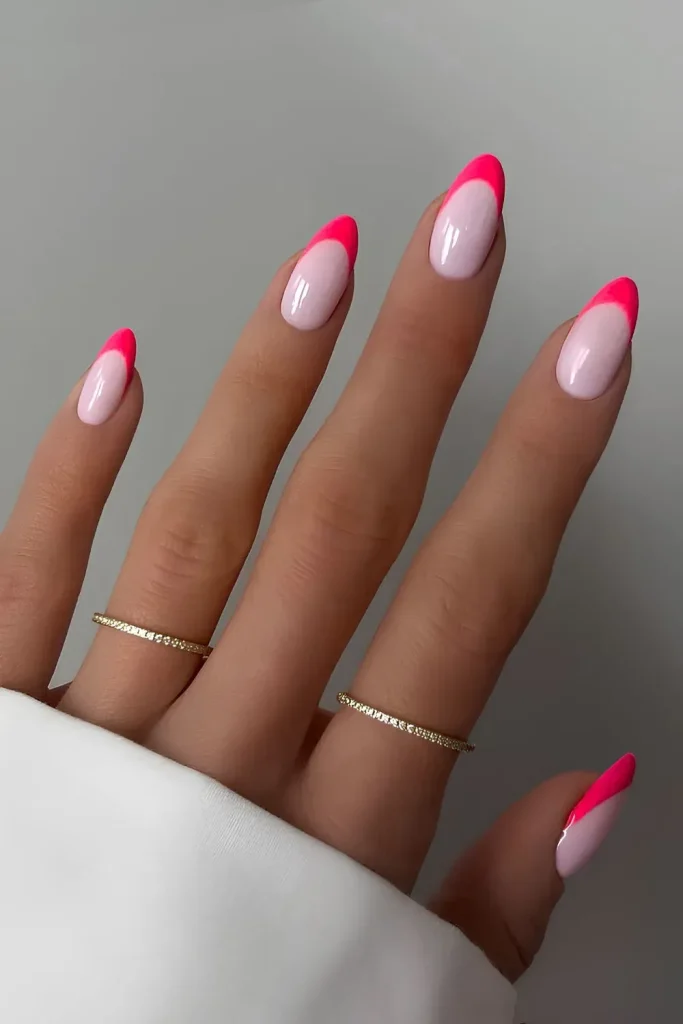 A close-up shot of two hands with long, almond-shaped nails featuring a bright pink French manicure.
