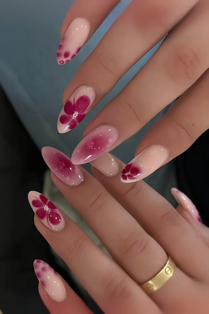 two hands with long, almond-shaped nails featuring a floral nail art design. 