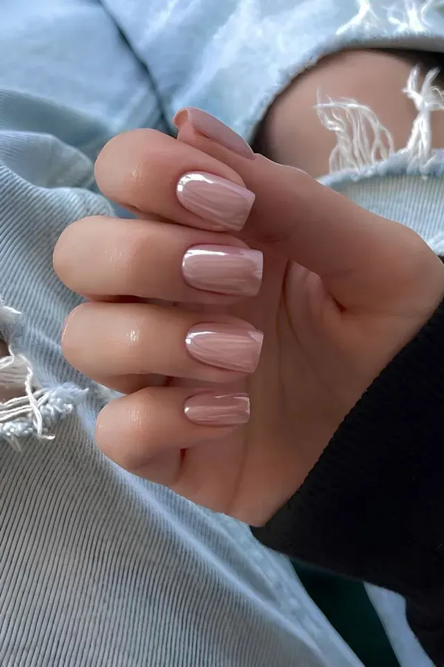 A hand showcasing cute pink nail designs, featuring glossy, soft pink nails with a smooth finish against ripped denim jeans.