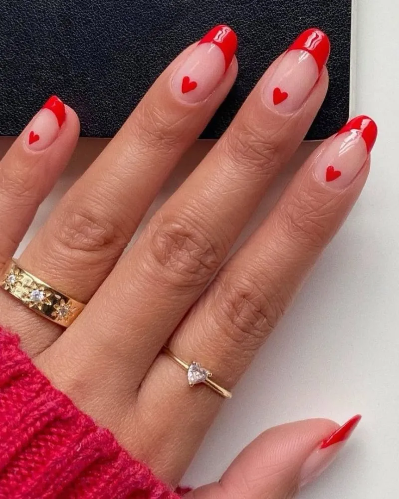 A stylish and creative nail design featuring a small red heart near the base of each nail.
