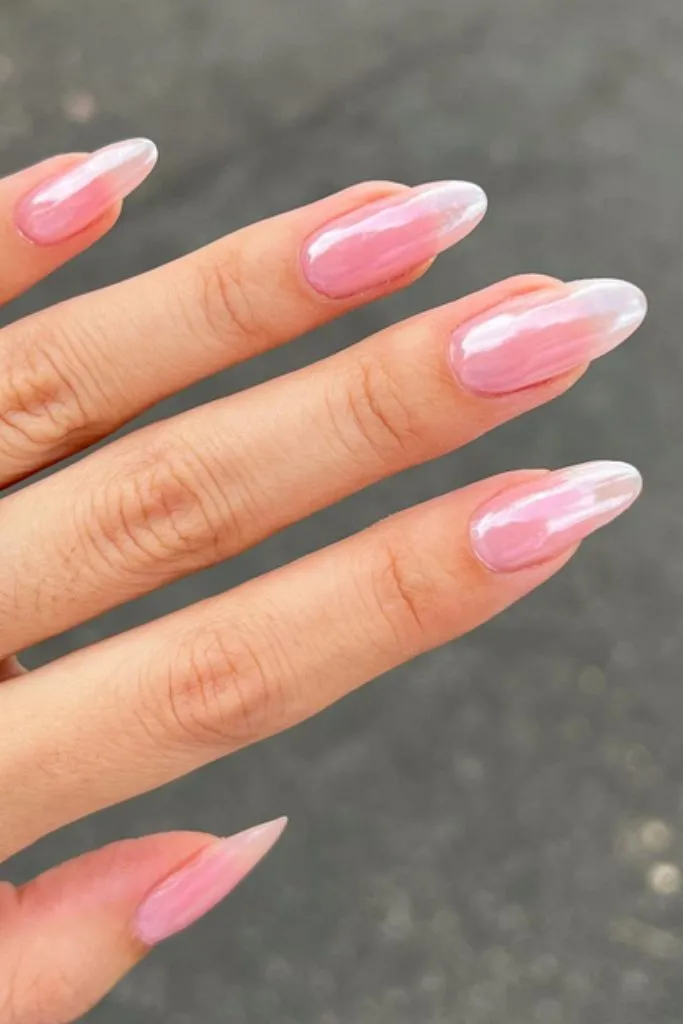 a hand with long, almond-shaped nails featuring a pink iridescent manicure