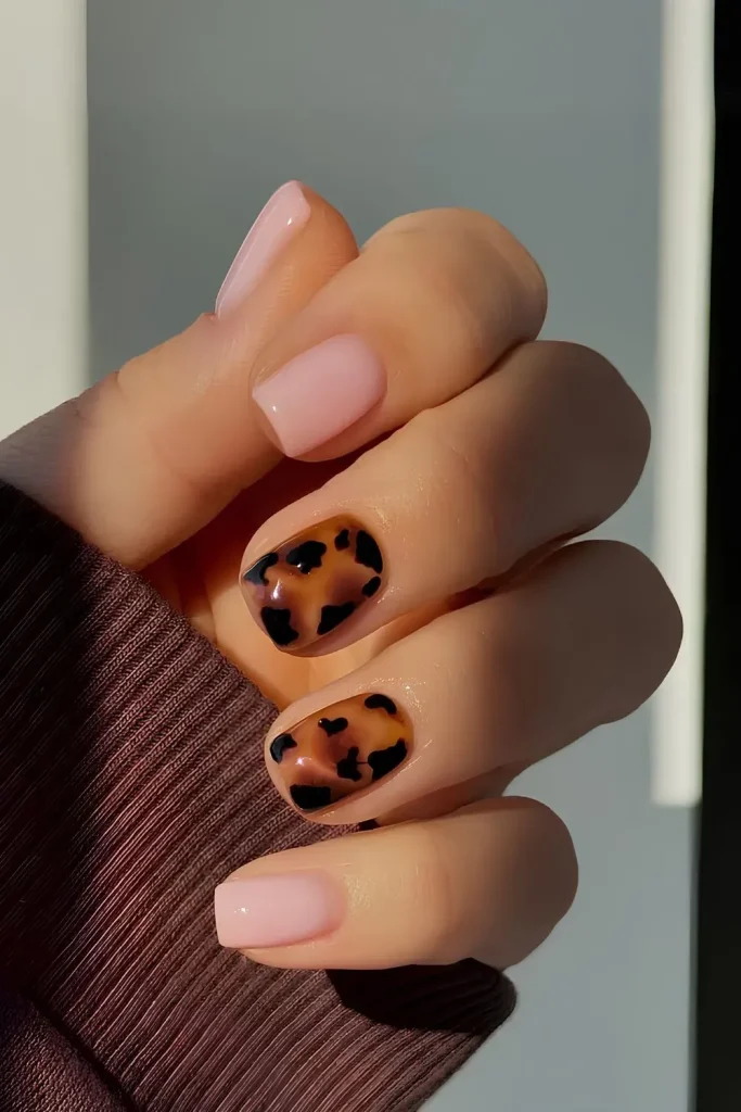 a chic manicure with soft nude-pink nails accented by two tortoiseshell-patterned nails, creating a stylish and modern look.