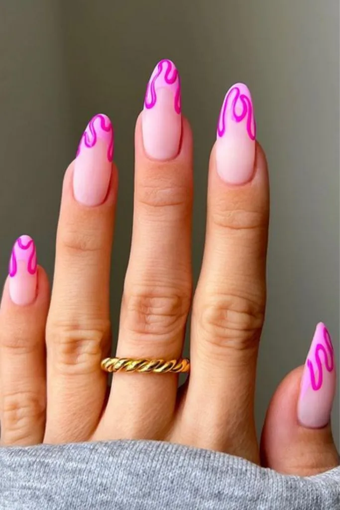 a hand with long, almond-shaped nails featuring a pink "dripping" design. 