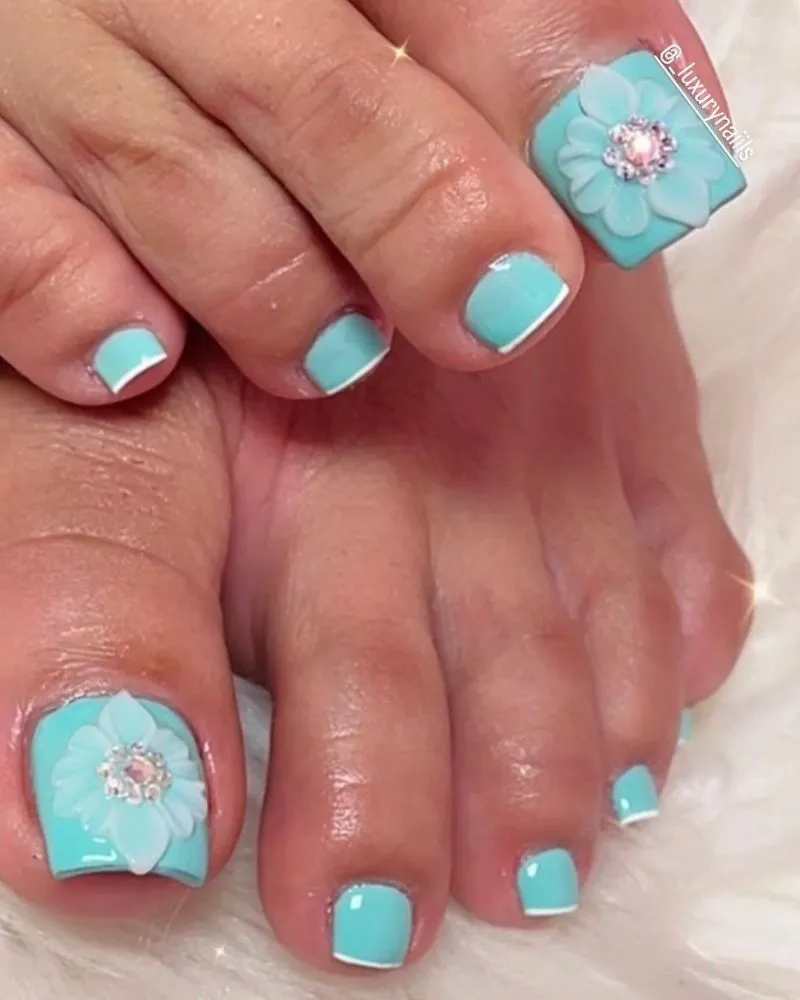 Elegant turquoise toenail design with 3D floral accents and rhinestone details for a chic summer look.