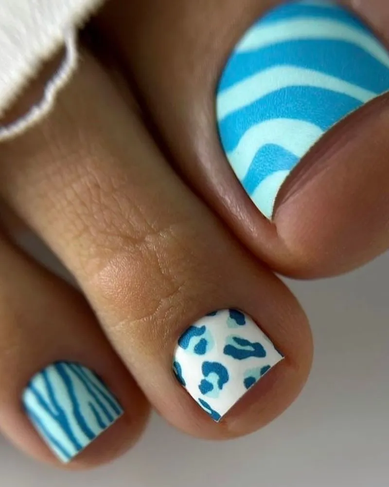 Stylish blue and white toenail design featuring zebra and leopard print patterns, creating a bold and trendy pedicure look