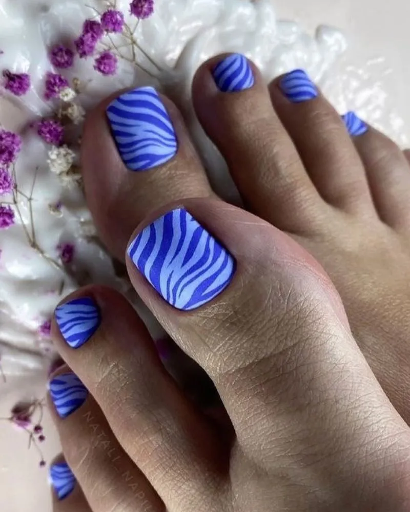 Vibrant blue and white zebra-striped toenail design, creating a bold and stylish summer look.