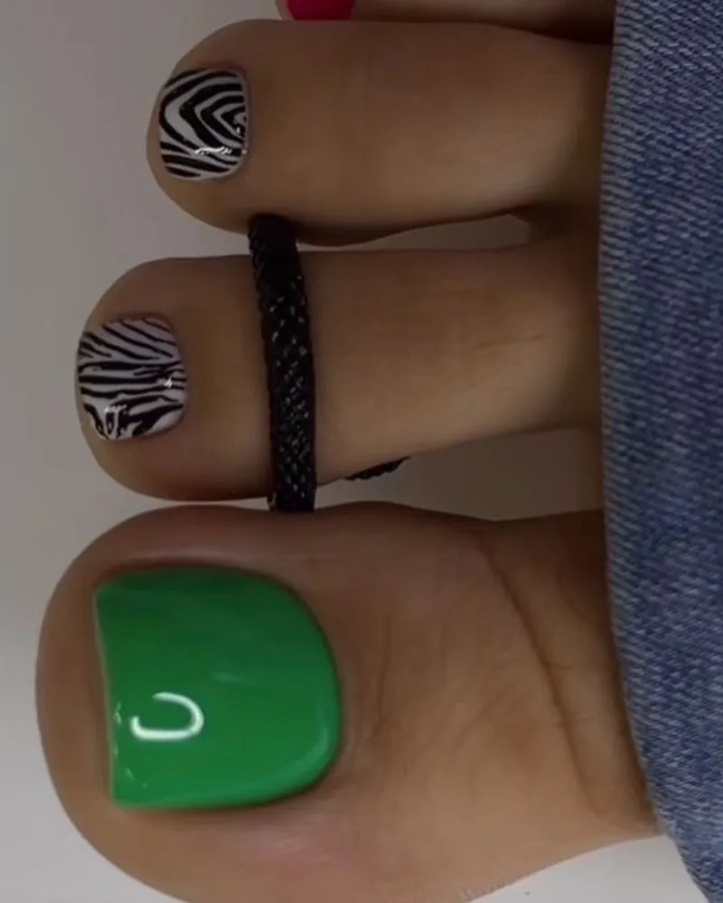 Trendy pedicure design with a bold green accent nail and stylish black-and-white zebra print on smaller toes, creating a chic and modern look.